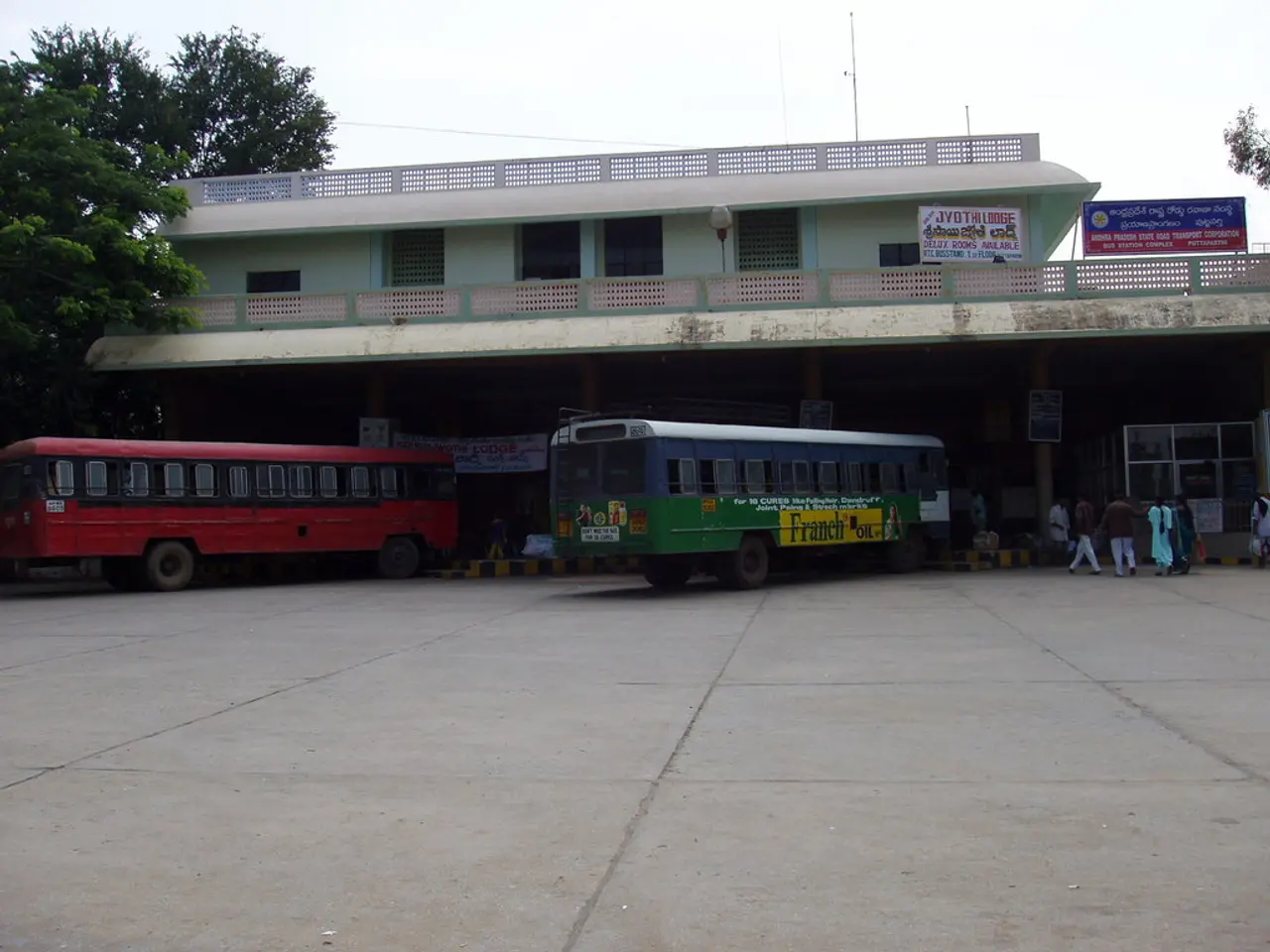 In this image we can see buildings, motor vehicles, persons on the road, advertisement boards, name...