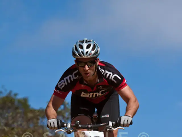 In this image we can see a man is cycling. He is wearing black color t-shirt, shorts and helmet....