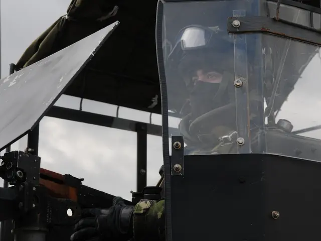 In this picture we can observe a person sitting in the vehicle, in front of a gun. He is wearing...