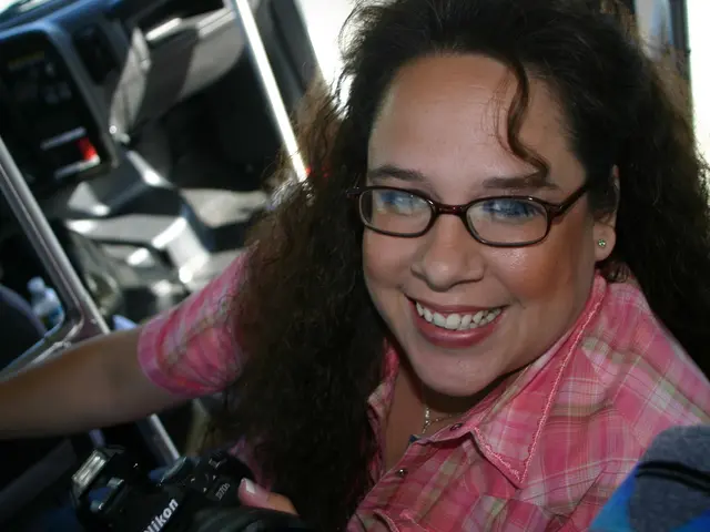 There is a woman in this picture smiling and she is wearing spectacles. She is holding a camera in...